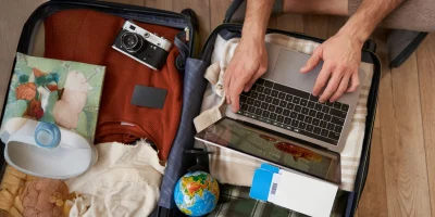 close-up-portrait-male-hands-using-laptop-top-opened-suitcase-man-packing-holiday